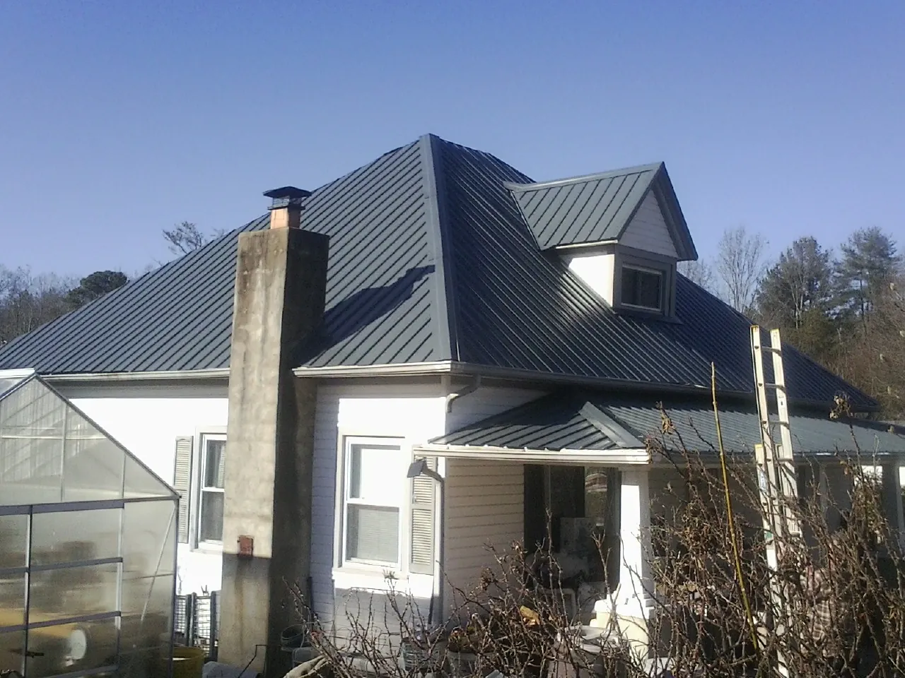 Dark blue standing seam metal roof on a white farmhouse with dormer — Slate & Tile Roof Repair by Roofing Brothers in Summerhill