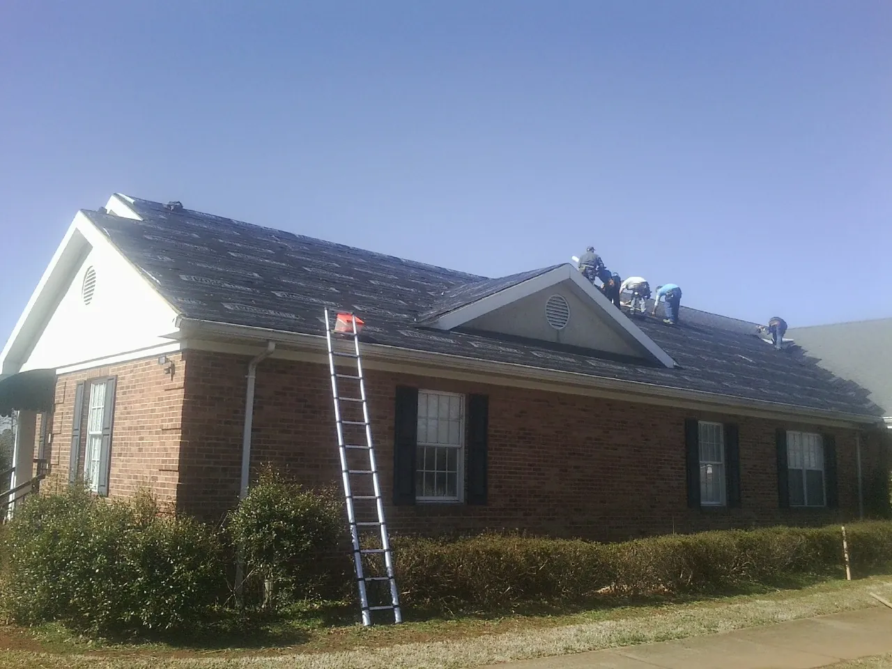 Crew tearing shingles off a brick ranch roof with a ladder set — Metal Roof Repair work by our crew in Summerhill