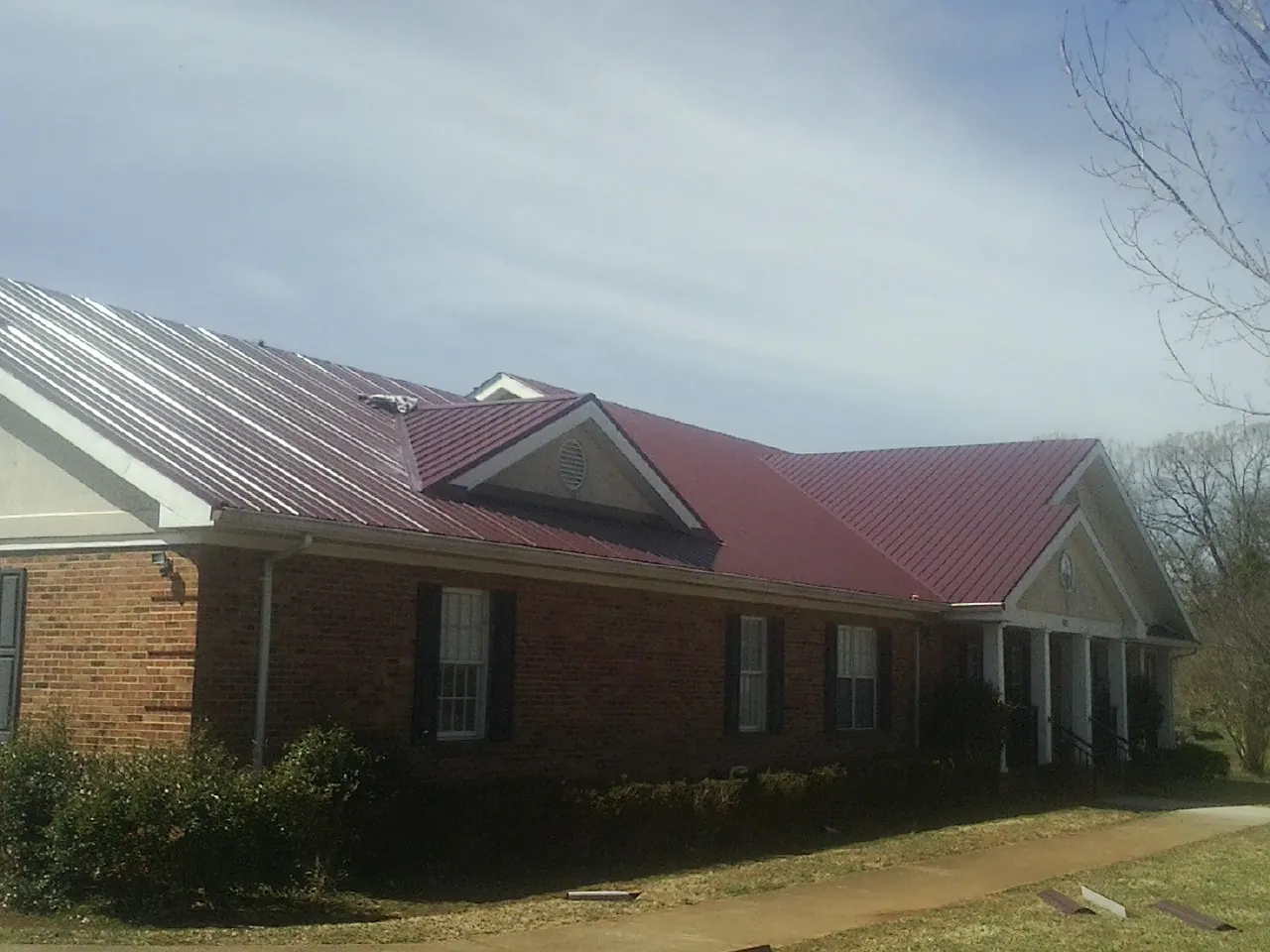 Red metal roof with gabled entries on a long brick building, from a Hail Damage Roof Repair job in Summerhill