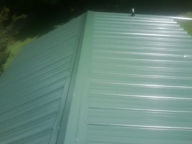 New green metal panels meeting at the ridge of a roof — Flat Roof Repair work by our crew in Summerhill