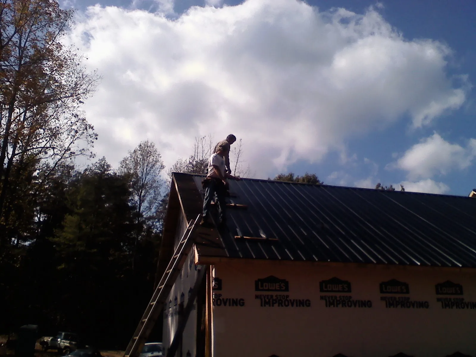 Roofer fastening dark metal panels high against a cloudy sky, from a Roof Inspection job in Summerhill