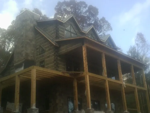 Stone chimney and dormers on a large log home with a timber porch in Summerhill