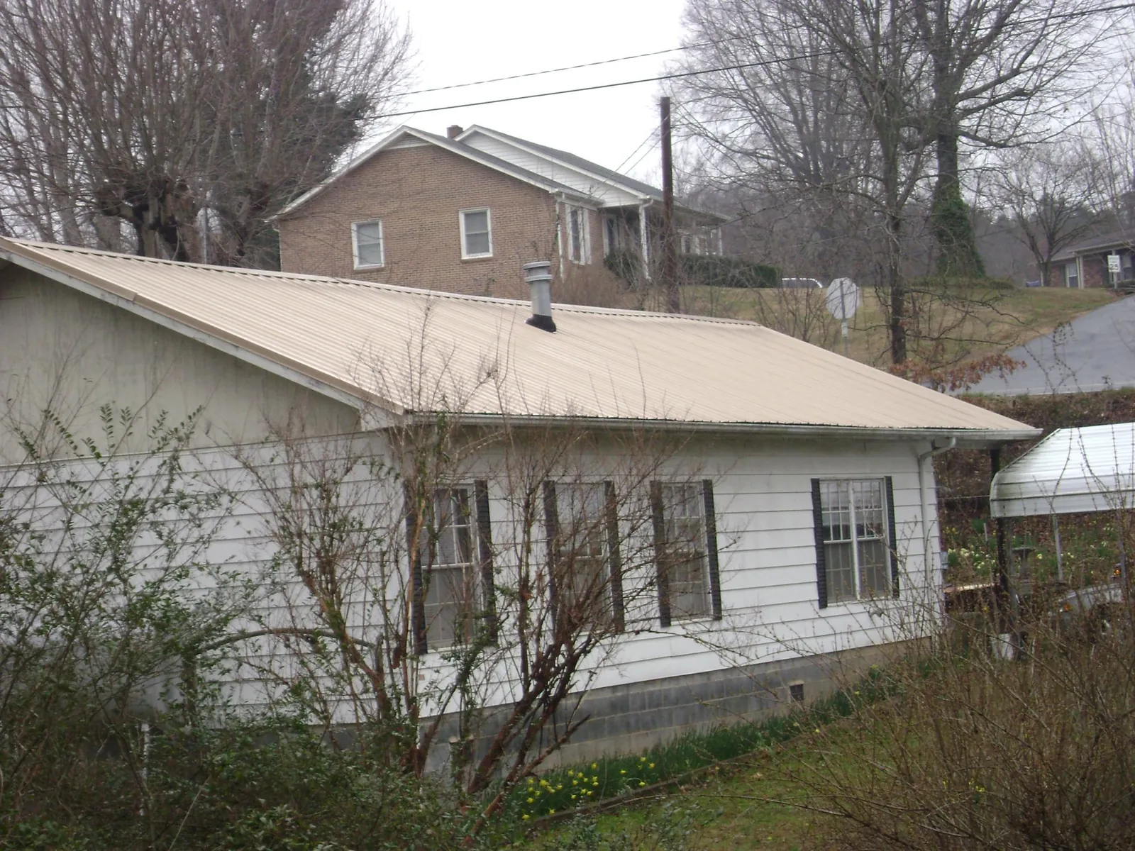 Tan metal roof on a white sided house set into a hillside — Commercial Roofing by Roofing Brothers in Summerhill