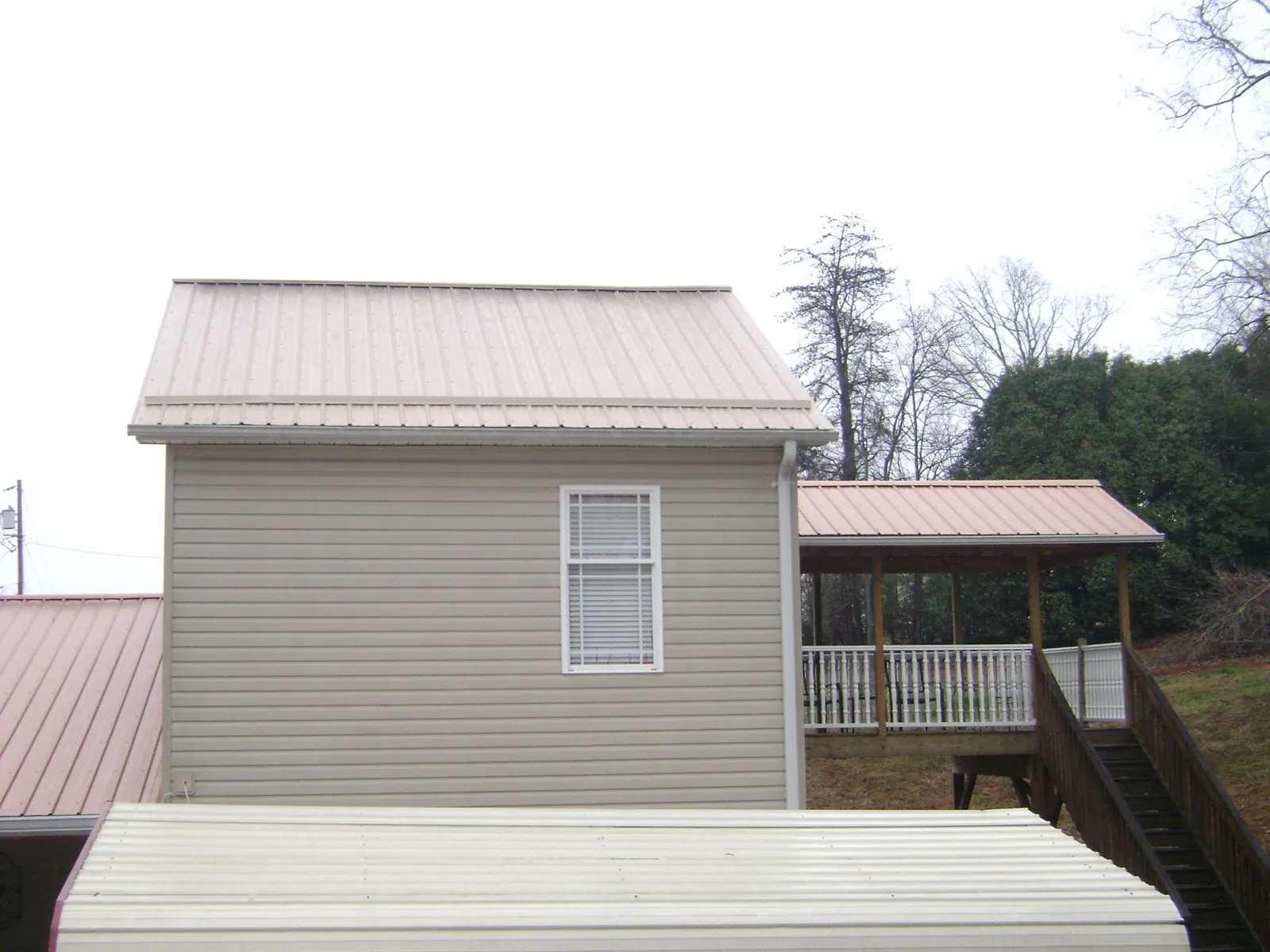 Tan metal roofs on a two story addition and attached porch, from a Roof Replacement job in Summerhill